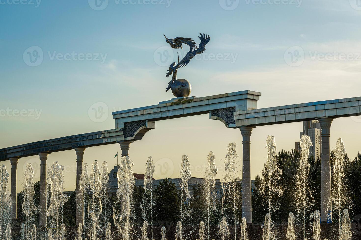 Denkmal und Reihen von Brunnen beleuchtet durch Sonnenlicht beim Sonnenuntergang oder Sonnenaufgang im das Unabhängigkeit Platz beim Sommer, Taschkent. foto