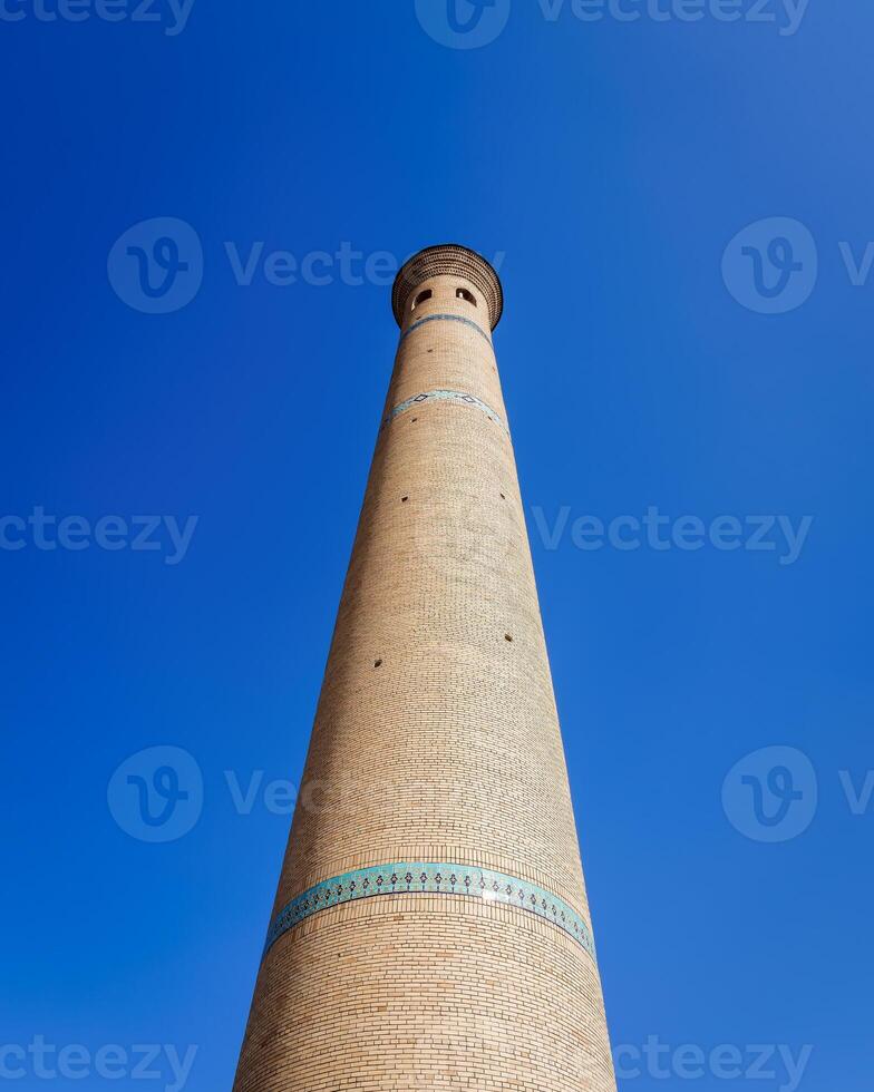 das Minarett von ein Backstein Moschee gegen ein Blau Himmel. foto