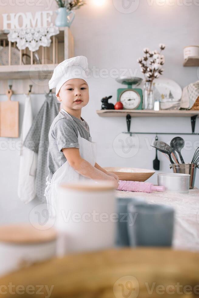 jung Junge süß auf das Küche Koch Koch im Weiß Uniform und Hut in der Nähe von Tisch. hausgemacht Lebkuchen. das Junge gekocht das Schokolade Kekse. foto
