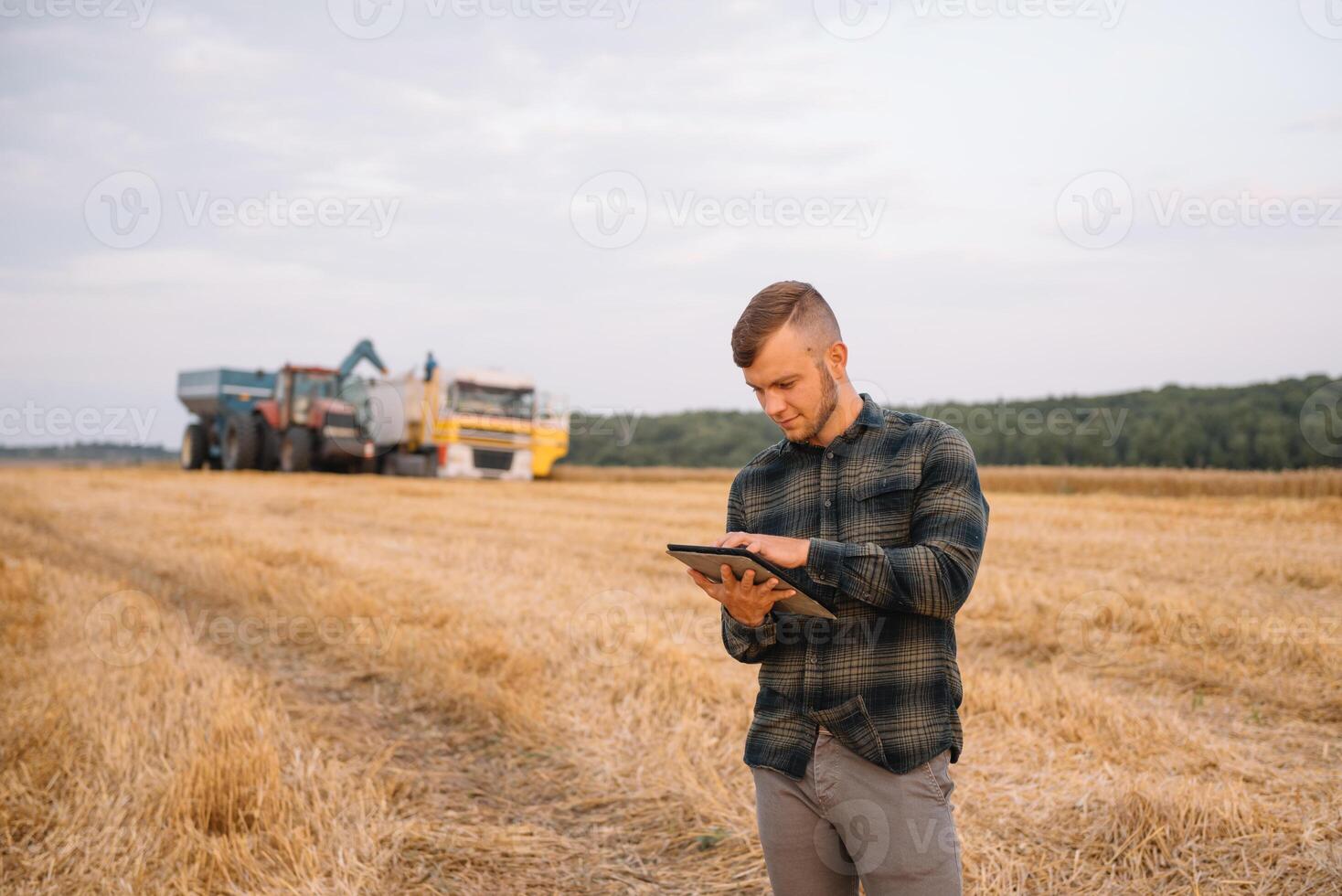 jung Agronom Mann Stehen auf Weizen Feld Überprüfung Qualität während kombinieren Mähdrescher Arbeiten foto