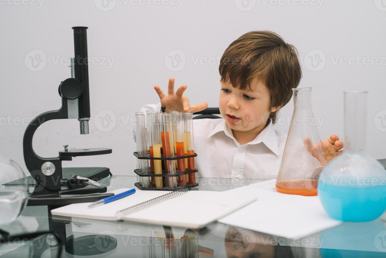 das Junge mit ein Mikroskop und verschiedene bunt Flaschen auf ein Weiß Hintergrund. ein Junge tun Experimente im das Labor. Explosion im das Labor. Wissenschaft und Bildung foto