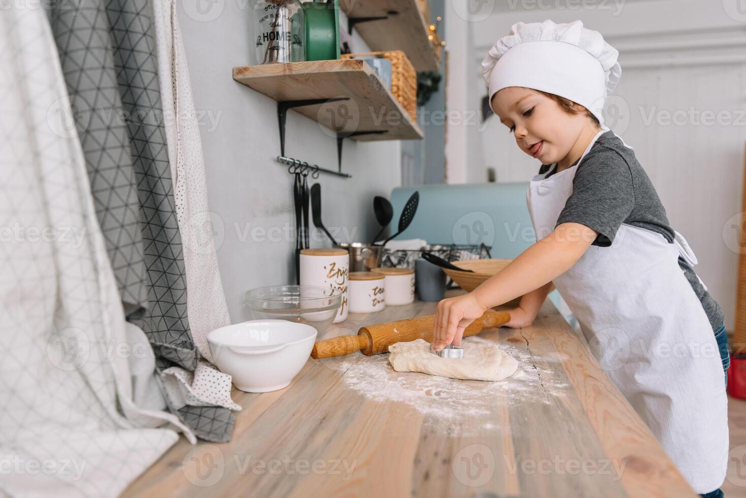 jung Junge süß auf das Küche Koch Koch im Weiß Uniform und Hut in der Nähe von Tisch. Weihnachten hausgemacht Lebkuchen. das Junge gekocht das Schokolade Kekse. foto