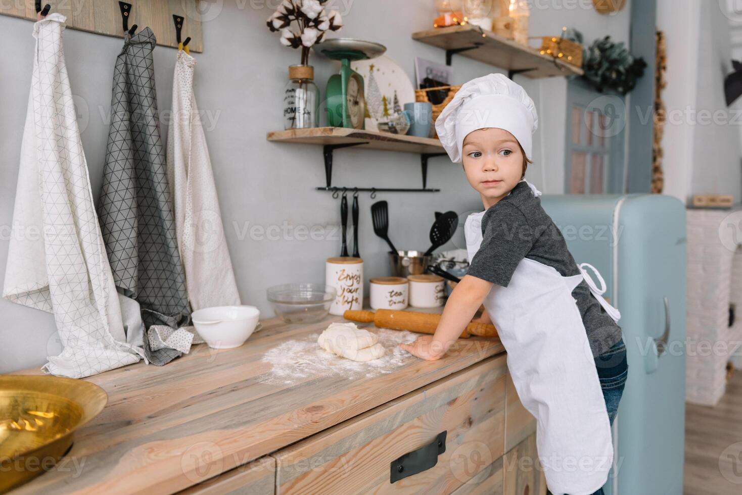 jung Junge süß auf das Küche Koch Koch im Weiß Uniform und Hut in der Nähe von Tisch. Weihnachten hausgemacht Lebkuchen. das Junge gekocht das Schokolade Kekse. foto