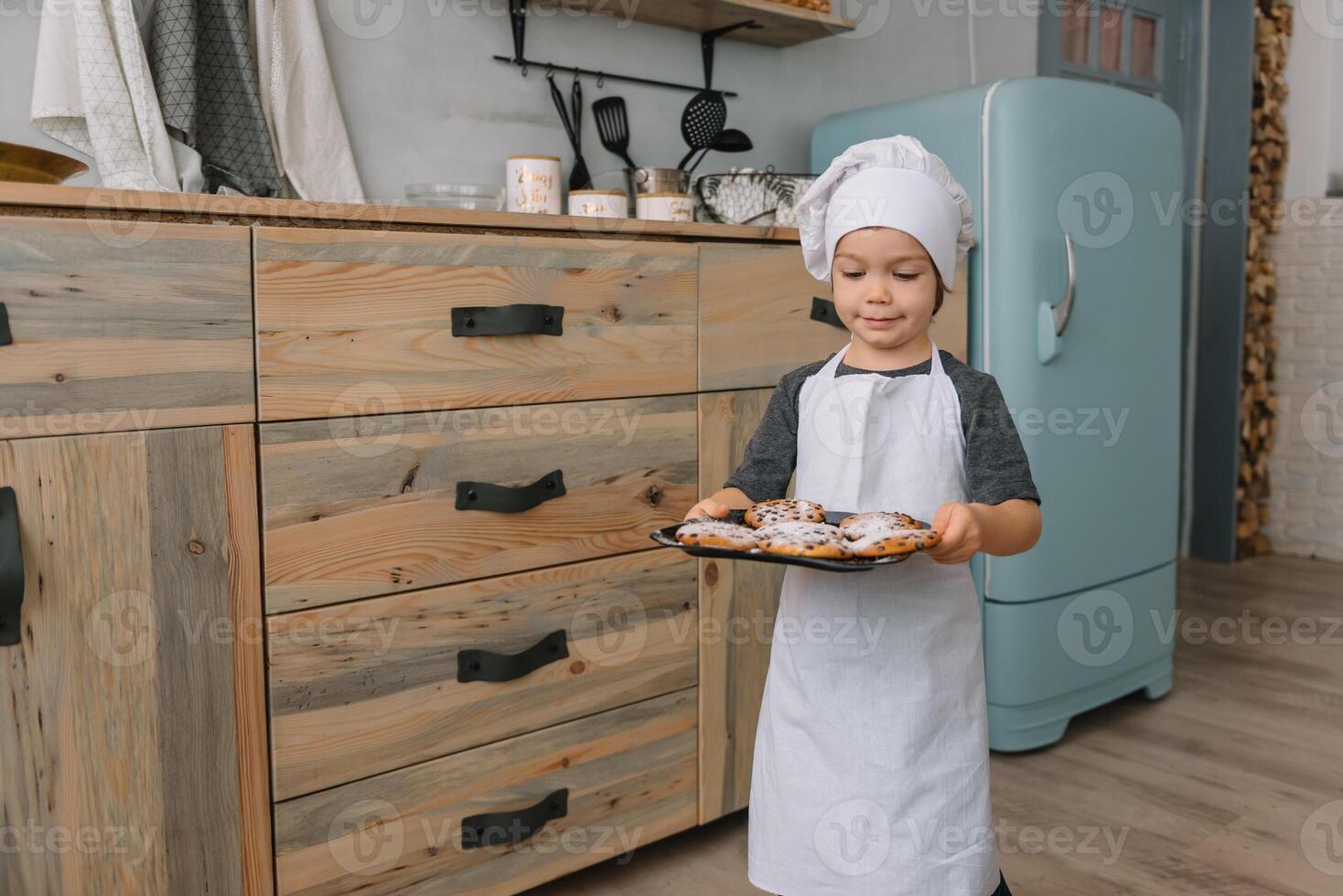 jung Junge süß auf das Küche Koch Koch im Weiß Uniform und Hut in der Nähe von Tisch. Weihnachten hausgemacht Lebkuchen. das Junge gekocht das Schokolade Kekse foto