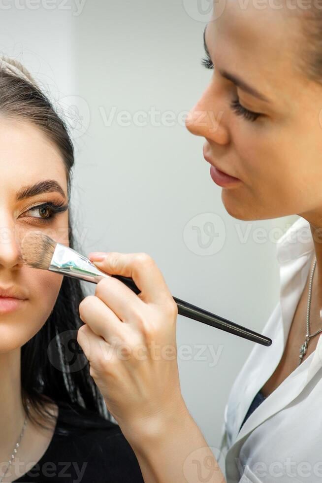 Nahansicht Porträt von ein Frau bewirbt sich trocken kosmetisch tonal Stiftung auf das Gesicht mit ein bilden Bürste. bilden Detail. foto