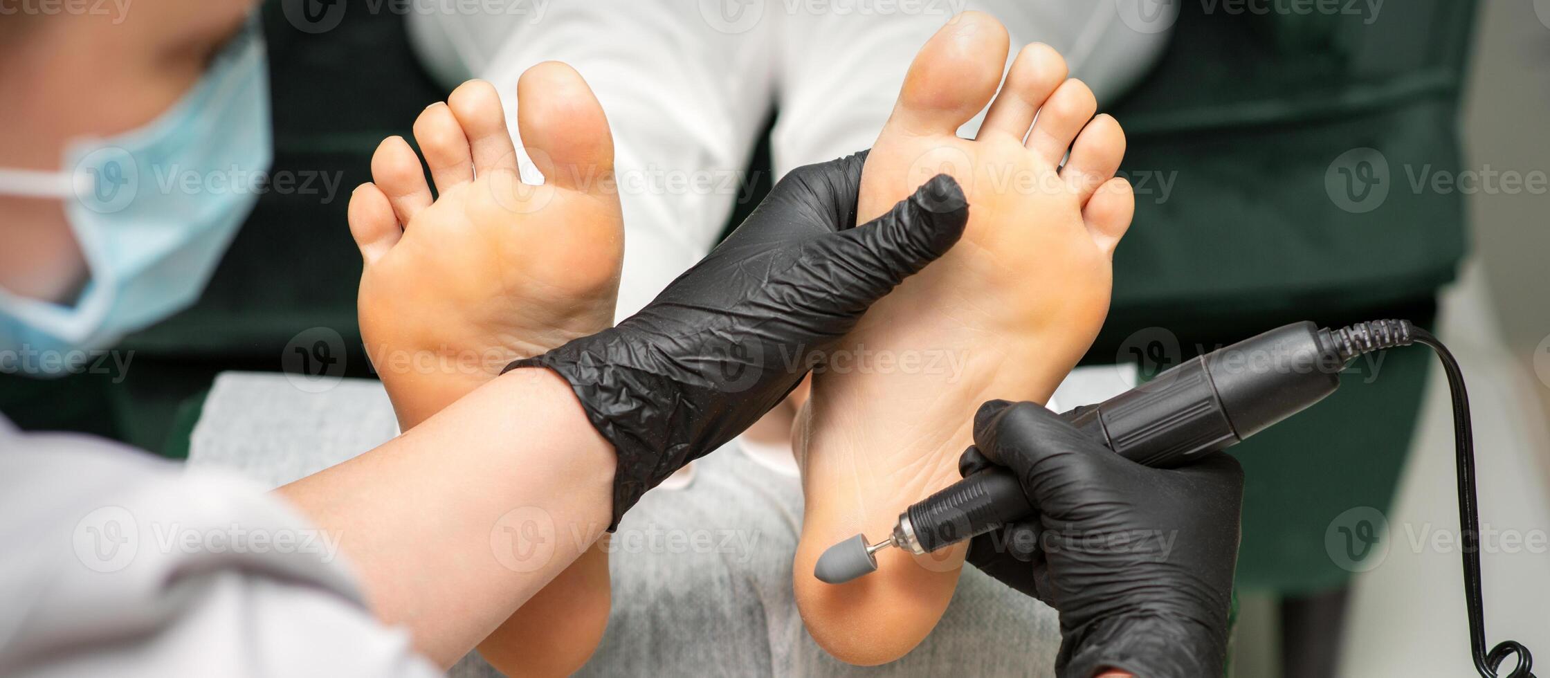 Peeling weiblich Füße. Hände von Podologie Spezialist im schwarz Handschuhe mit Besondere Mahlen Ausrüstung Polieren weiblich Fuß von Kallus und Mais im das Schönheit Salon. foto