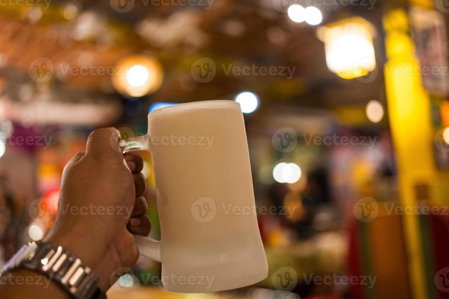 Becher von Bier im gefroren Becher im das Mann Hand gegen das Kneipe verwischen Hintergrund foto
