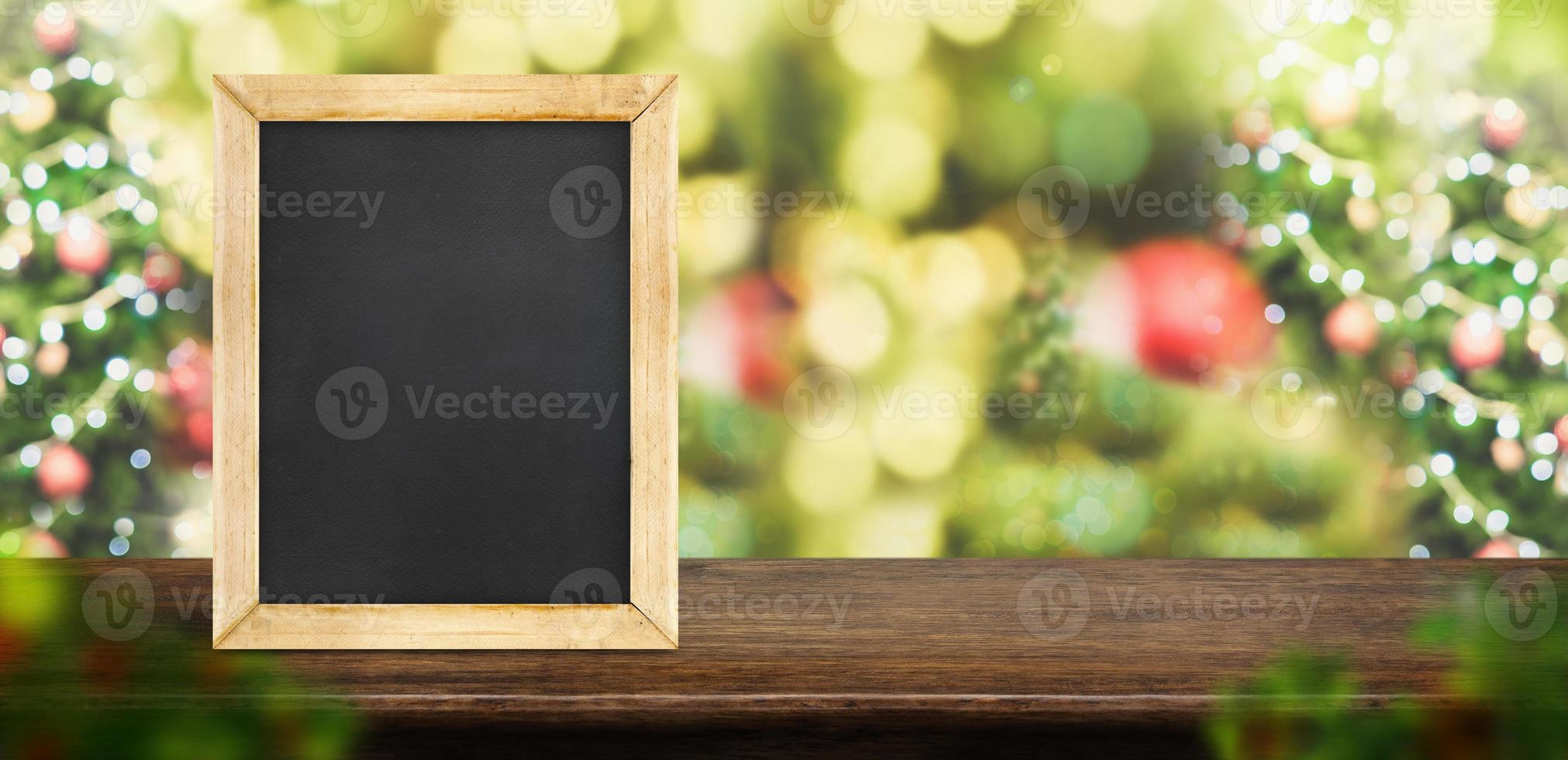 Tafel auf dunkelbrauner Holztischplatte mit abstraktem Unschärfe-Weihnachtsbaum foto
