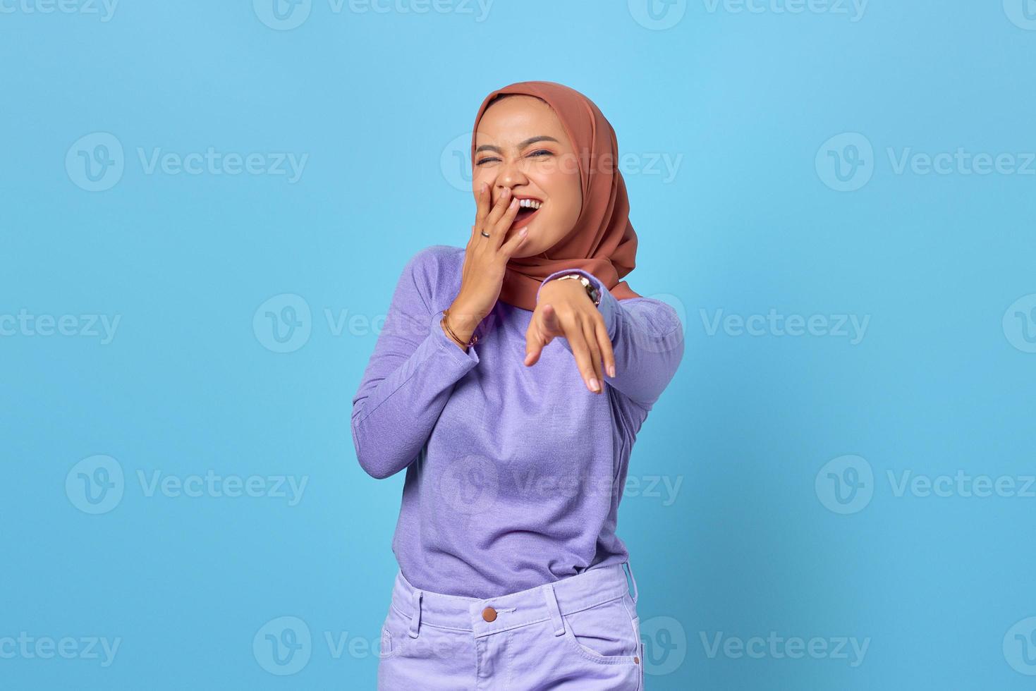 Porträt einer fröhlichen jungen asiatischen Frau, die mit dem Finger auf die Kamera auf blauem Hintergrund zeigt foto