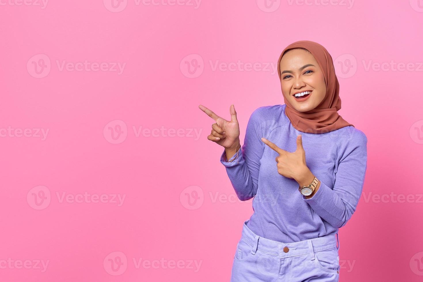 Porträt einer lächelnden jungen asiatischen Frau, die mit dem Finger auf den Kopierraum auf rosafarbenem Hintergrund zeigt foto