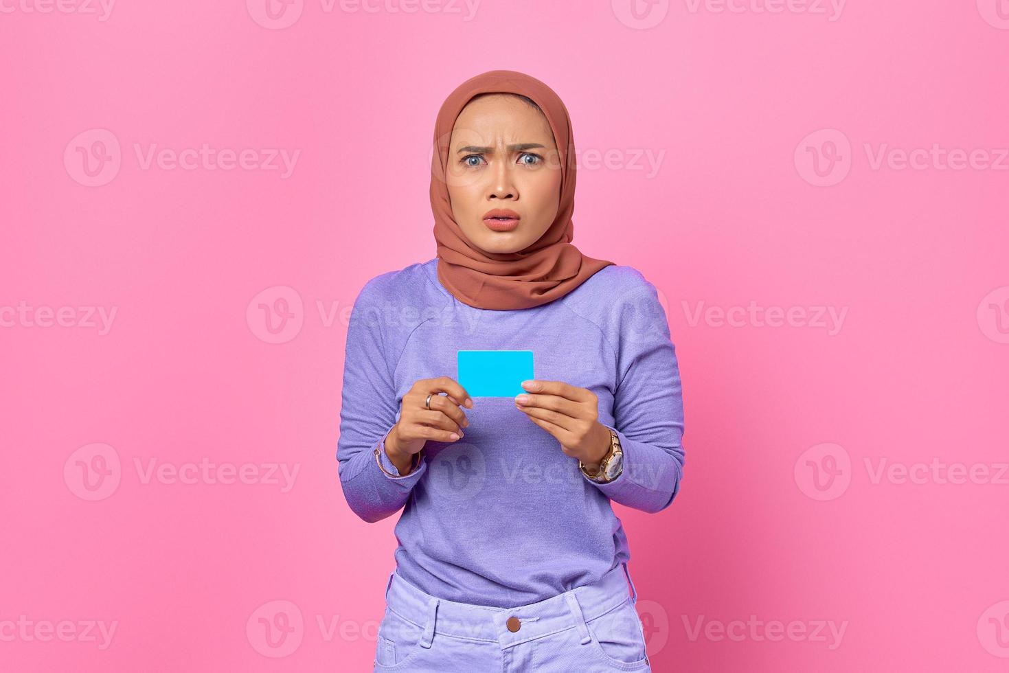 Porträt einer schockierten jungen Asiatin, die Kreditkarte auf rosa Hintergrund zeigt foto