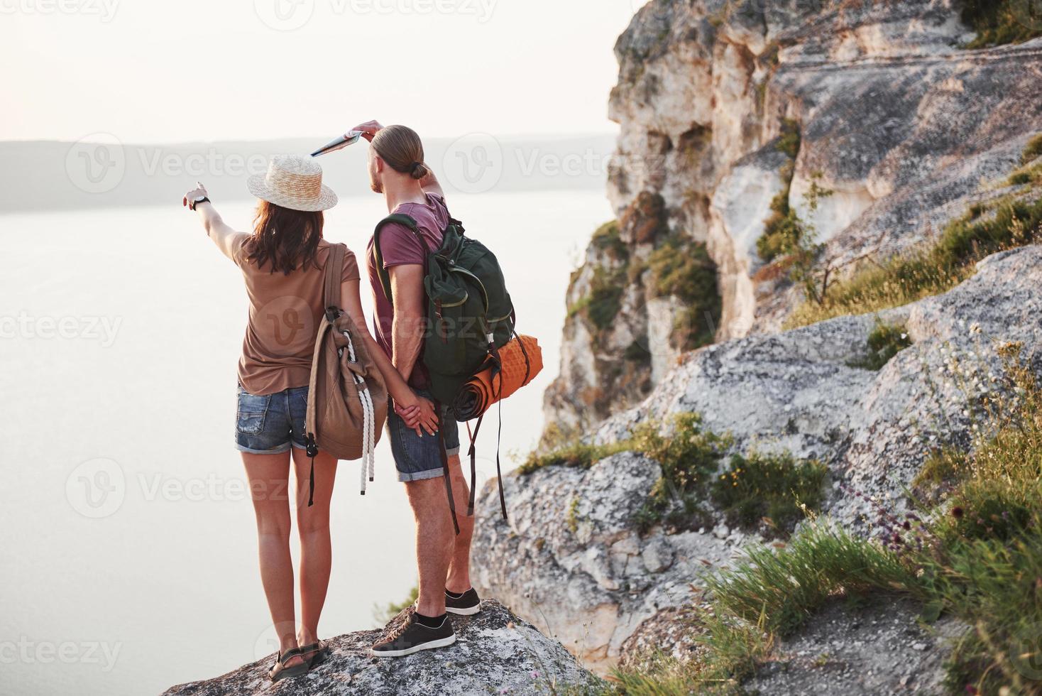 Zwei touristische Männer und Frauen mit Rucksäcken stehen an der Spitze des Felsens und genießen den Sonnenaufgang. Reisen durch Berge und Küste, Freiheit und aktives Lifestyle-Konzept foto