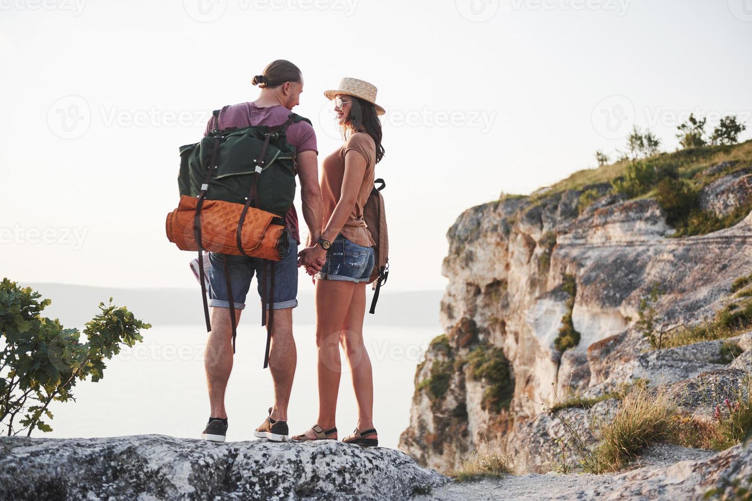 Zwei touristische Männer und Frauen mit Rucksäcken stehen auf dem Gipfel des Berges und genießen den Sonnenaufgang. Reise-Lifestyle-Abenteuer-Urlaub-Konzept foto