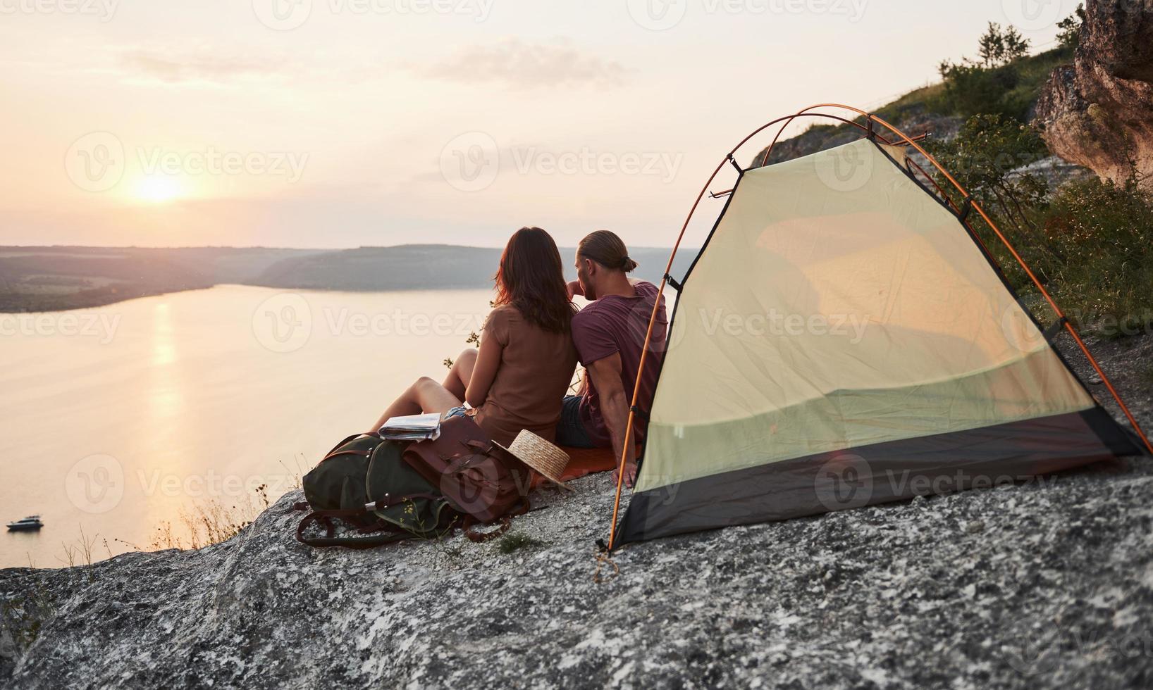 Foto eines glücklichen Paares, das während der Wanderung im Zelt mit Blick auf den See sitzt. Reise-Lifestyle-Abenteuer-Urlaub-Konzept