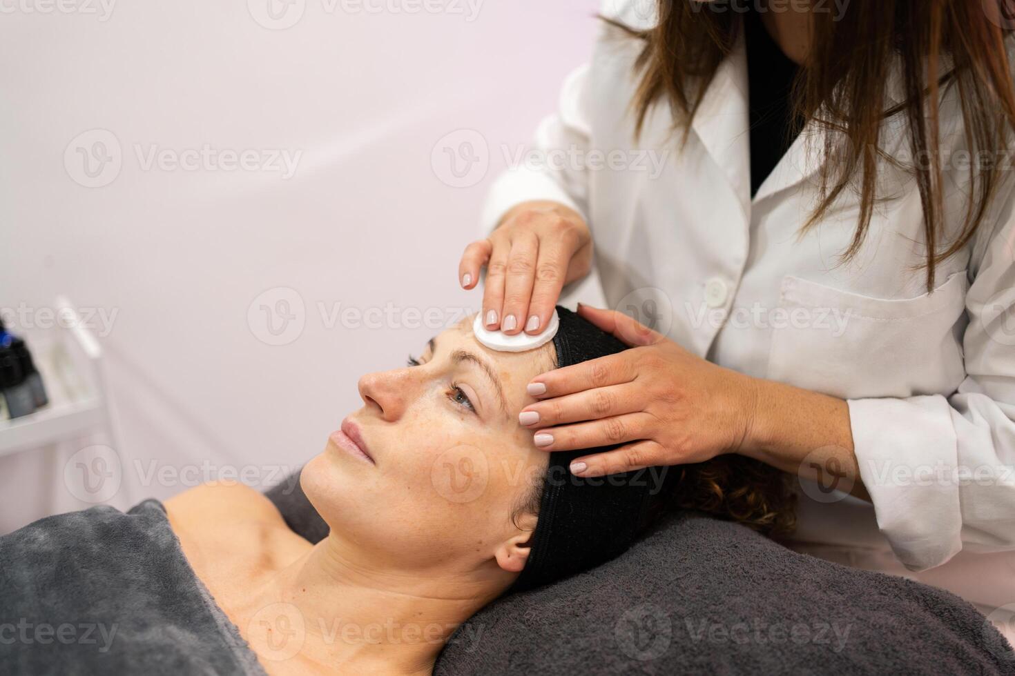 Ernte Kosmetikerin mit Haut Pflege Baumwolle Pad auf Gesicht von Klient im Schönheit Salon foto