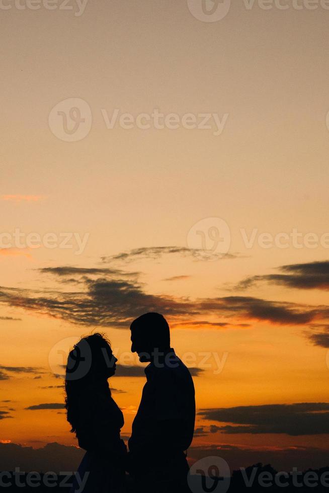 Silhouetten eines glücklichen jungen Paares und eines Mädchens auf einem Hintergrund von orangefarbenem Sonnenuntergang foto