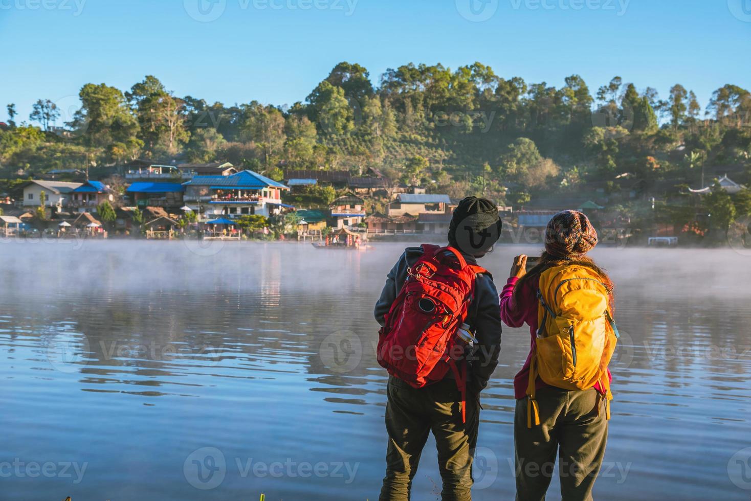 ein asiatisches paar, das morgens steht und den nebel auf dem see aufsteigt. reiseverbot rak thai dorf, mae hong son in thailand. mach ein foto vom see