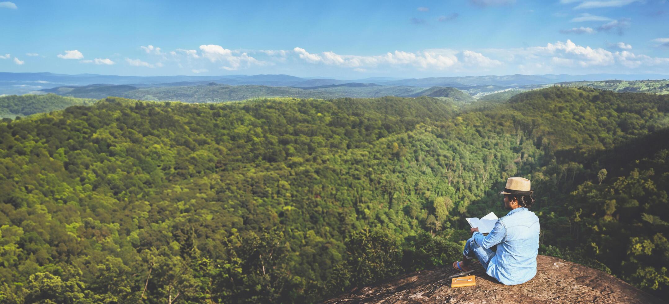 asiatische Mannreisen entspannen sich im Urlaub. Sitze entspannen, Bücher lesen auf felsigen Klippen. auf dem Berg. in Thailand foto