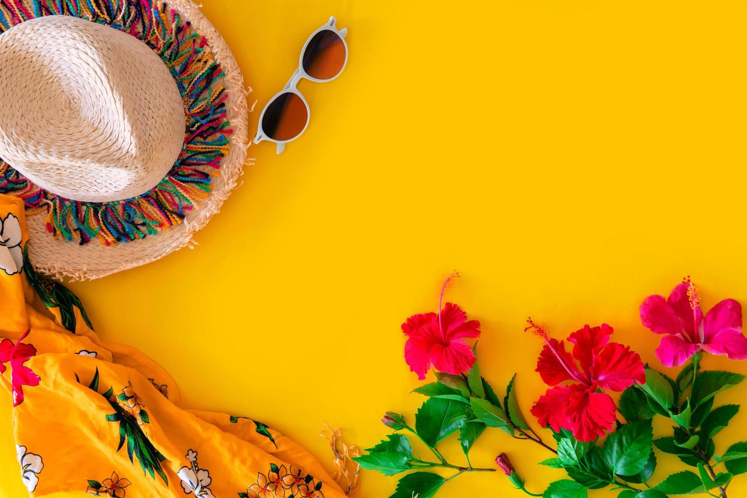 Strandaccessoires für den Reisenden auf gelbem Hintergrund - Sonnenbrille, Strohhut und Hibiskusblüten. Strandtourismuskonzept. Sommer foto