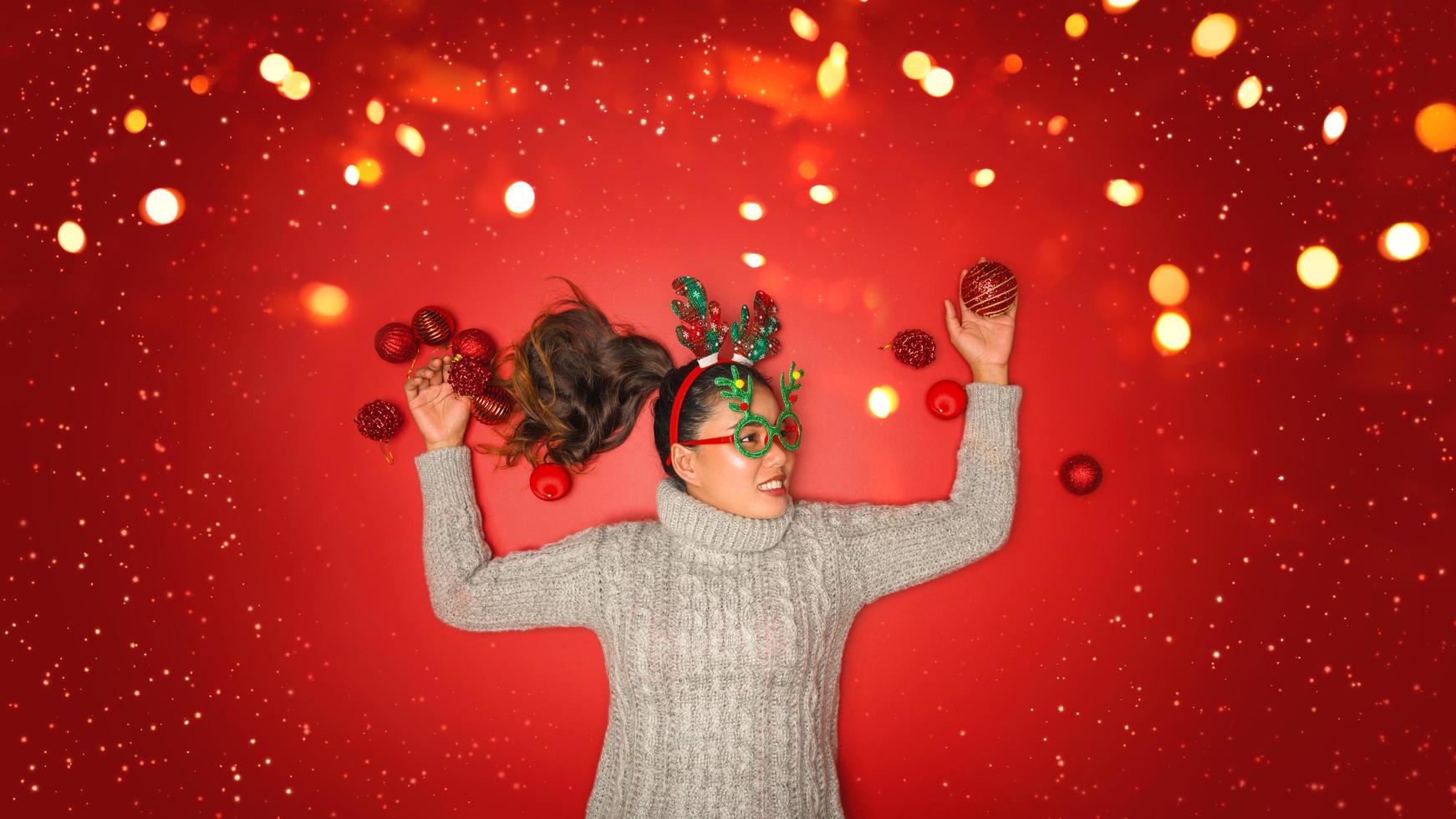 Weihnachten neues Jahr. junge Frau, gekleidet in warmen Pullover mit Requisiten Ball rot mit Weihnachtsschmuck im Urlaub auf glänzendem rotem Hintergrund. Konzept Frohe Weihnachten. foto