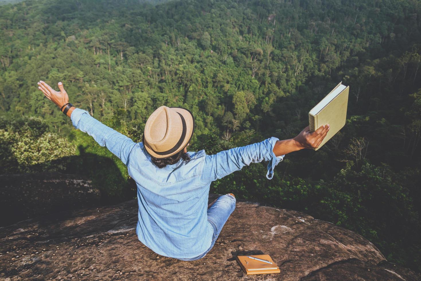 asiatische Mannreisen entspannen sich im Urlaub. Sitze entspannen, Bücher lesen auf felsigen Klippen. auf dem Berg. in Thailand foto