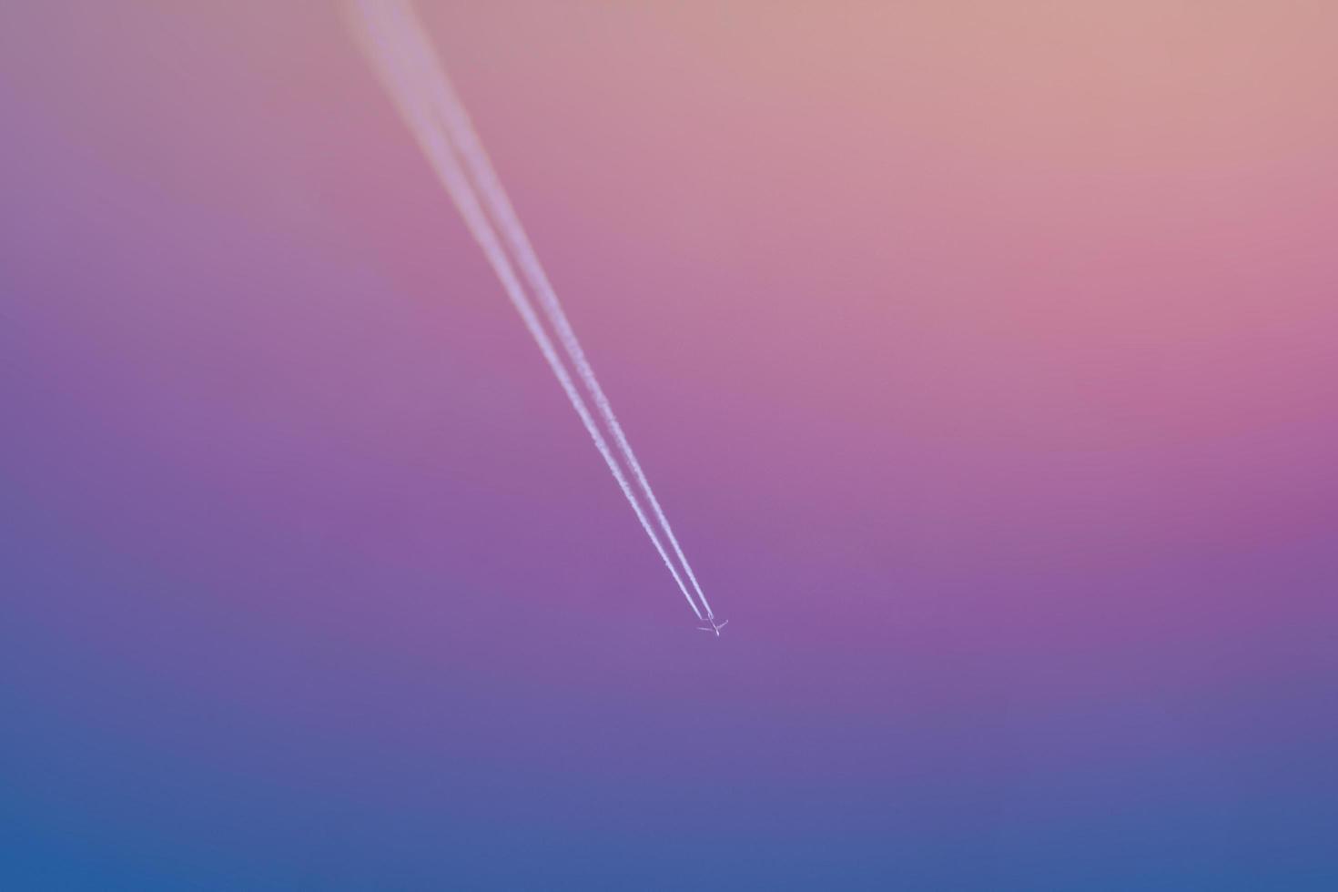 Flugzeug mit einem weißen Zug gegen Sonnenunterganghimmel. foto