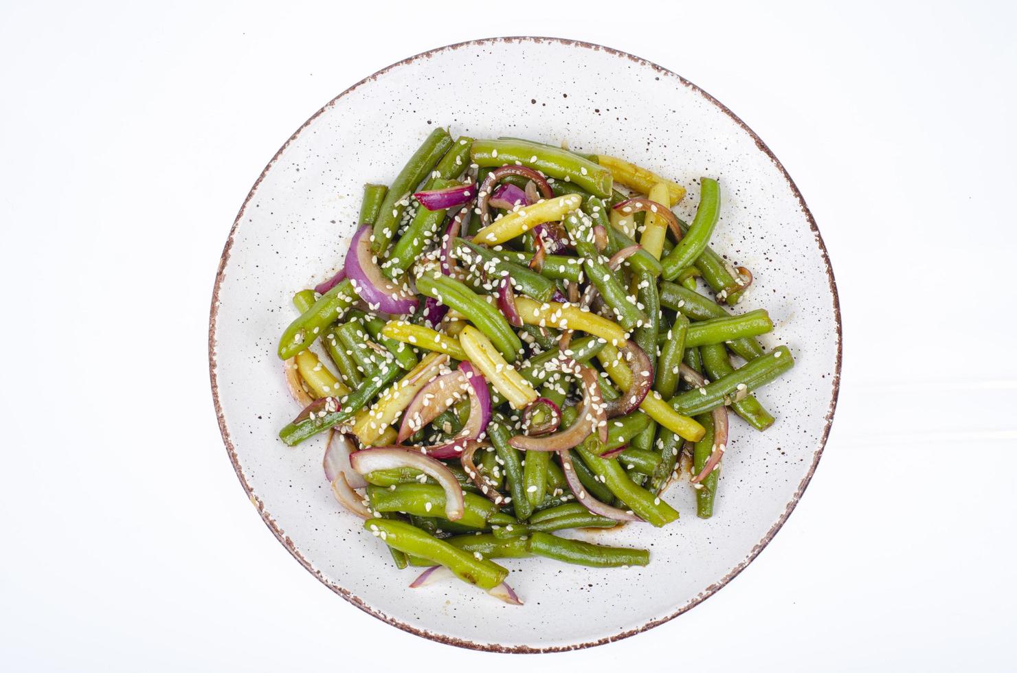 vegetarisches Gericht aus grünen Bohnen mit roten eingelegten Zwiebeln und Sesam. Studiofoto foto