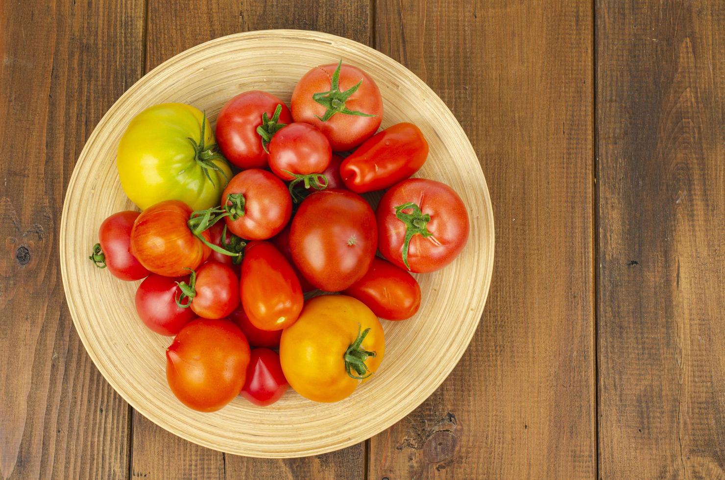 große hölzerne Bambusschale mit reifen Tomaten. Studiofoto. foto