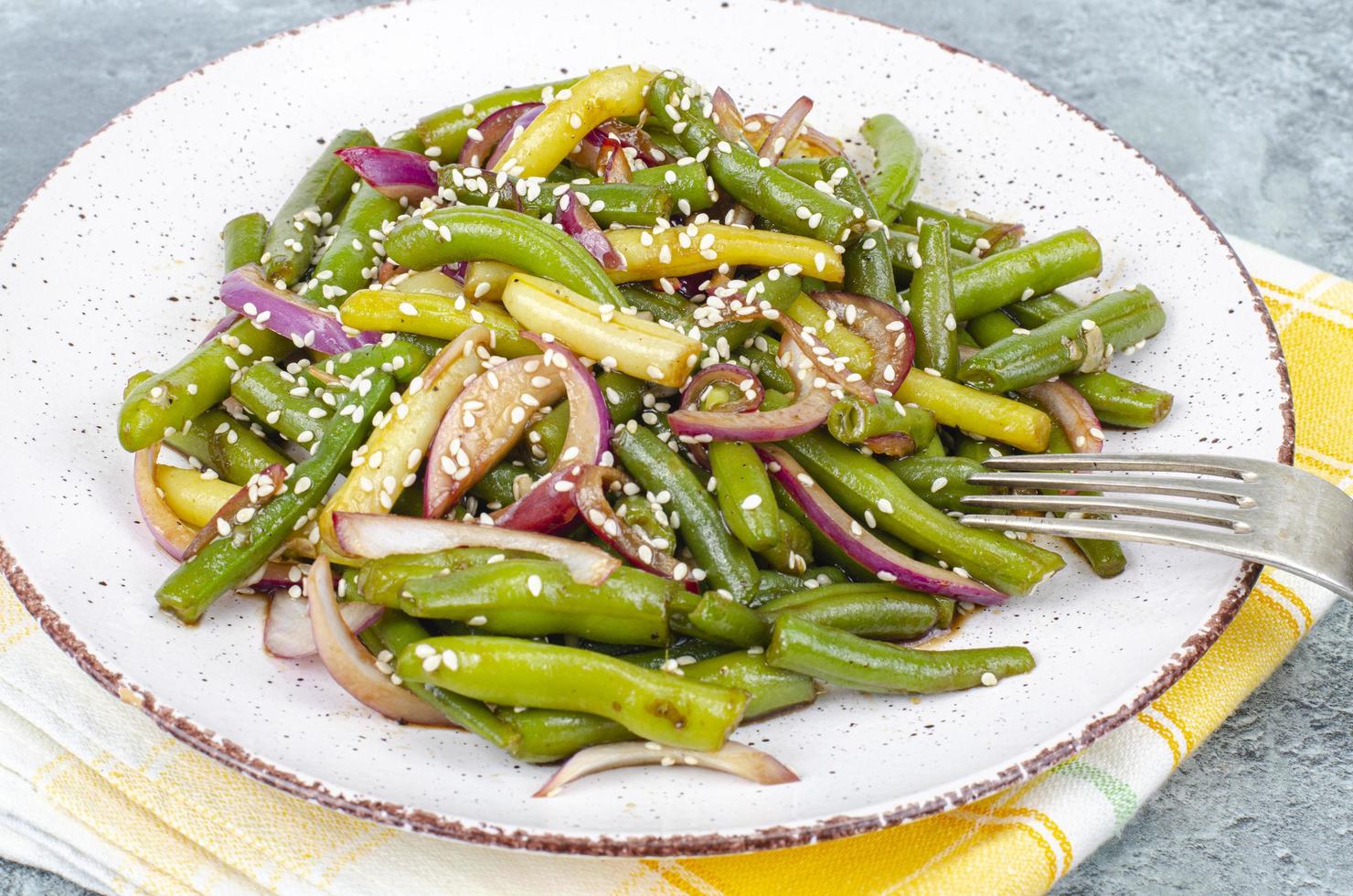 vegetarisches Gericht aus grünen Bohnen mit roten eingelegten Zwiebeln und Sesam. Studiofoto foto