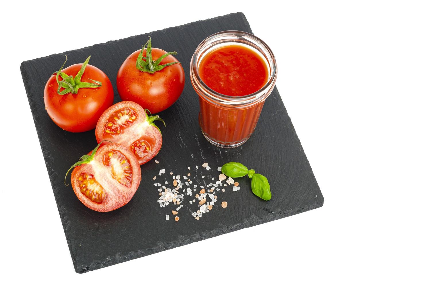 Glas Tomatensaft, reife rote Tomaten auf schwarzem Steintablett foto