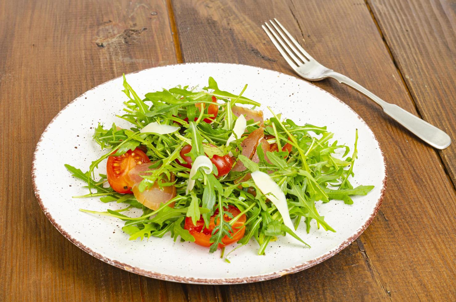 Gericht aus Rucola, Tomaten, Trockenfleisch und Käse. Salat auf Teller auf Holzuntergrund foto