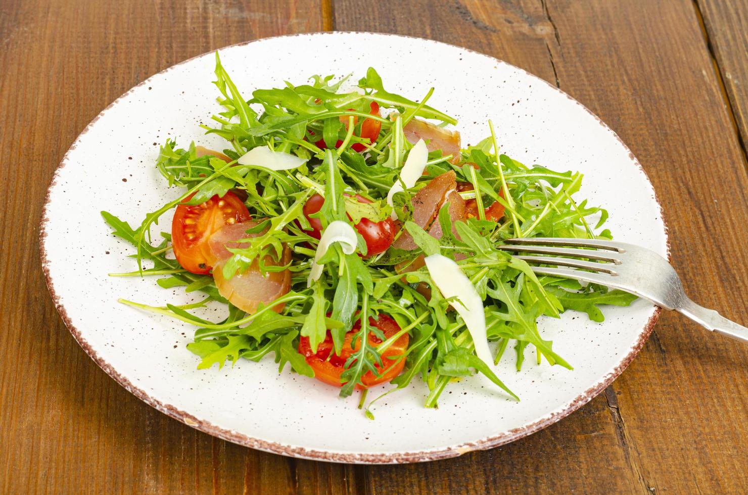 Gericht aus Rucola, Tomaten, Trockenfleisch und Käse. Salat auf Teller auf Holzuntergrund foto