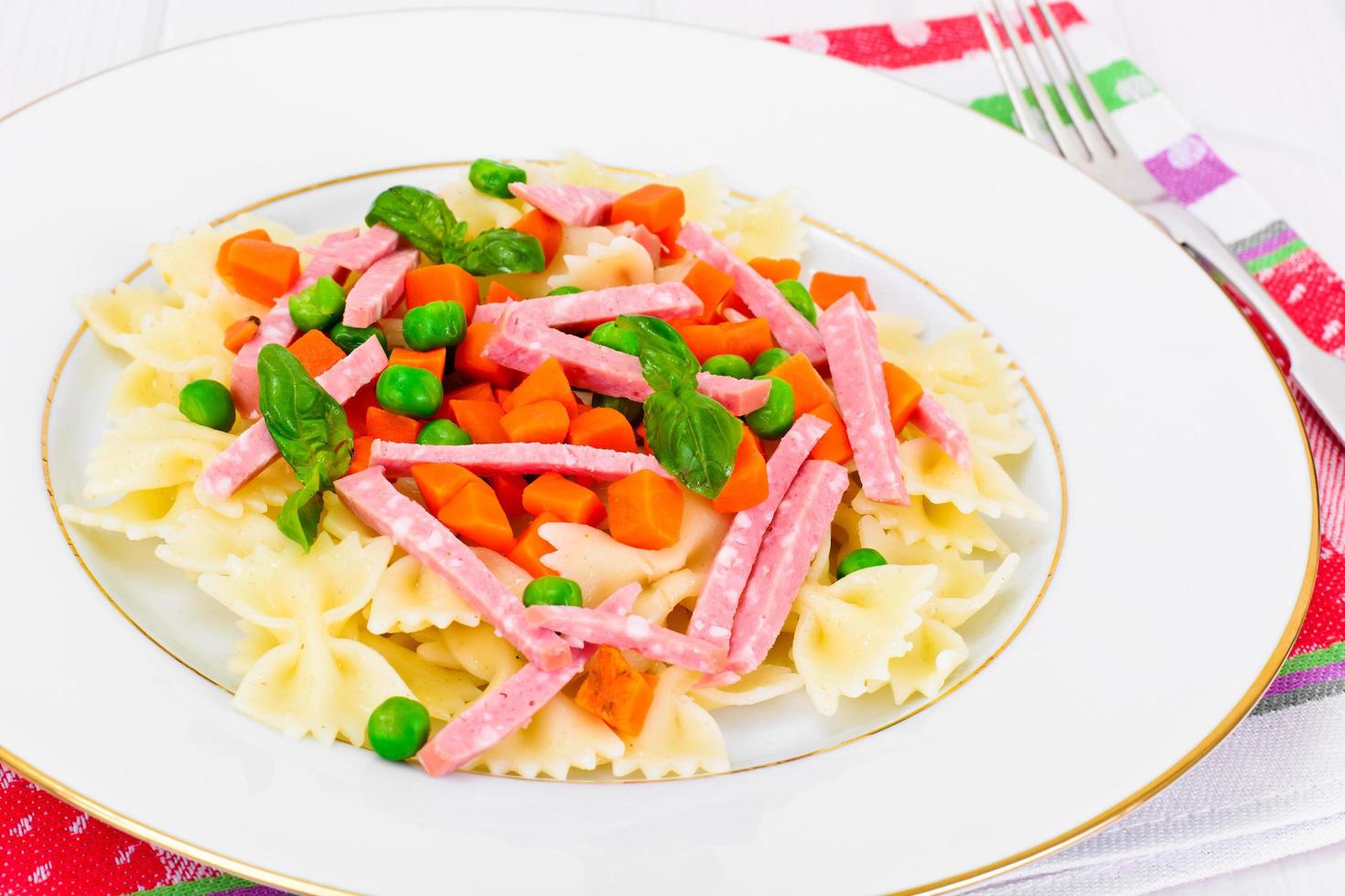 Nudelbogen mit gewürfelten Karotten, Salami und grünen Erbsen foto