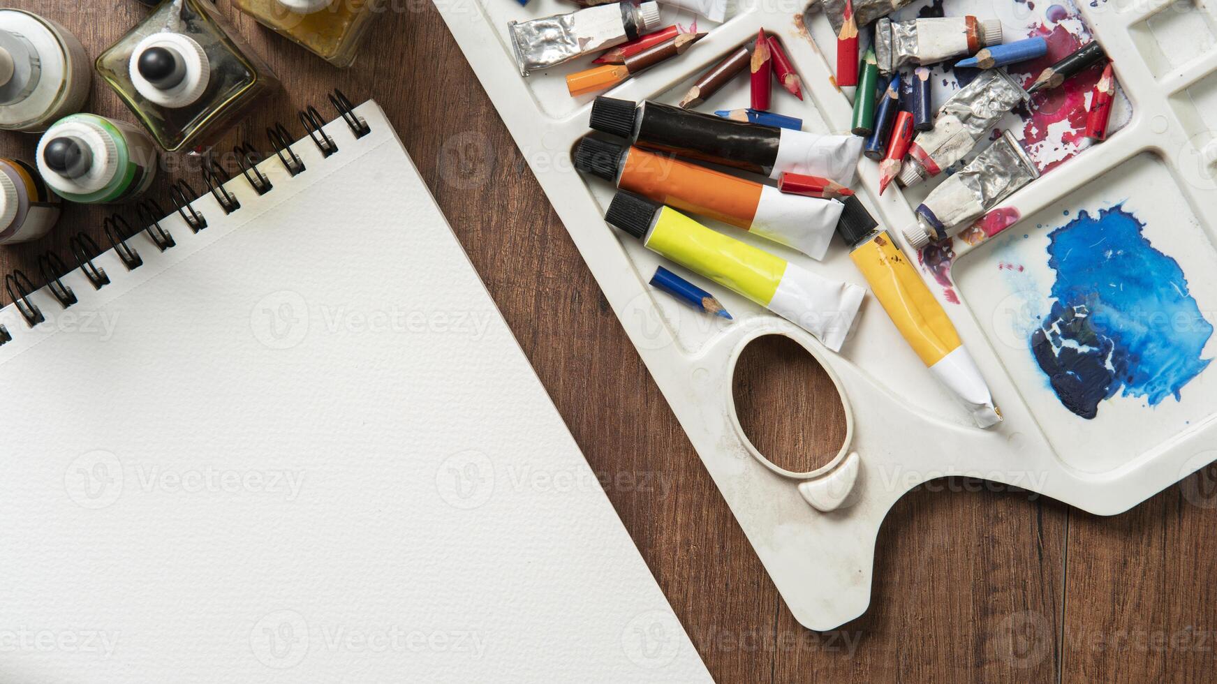 oben Aussicht von hölzern Tabelle mit Bleistifte, Farbe Rohre, Kunst Lieferungen, Tinte Flaschen, Vielfalt von Bürsten foto