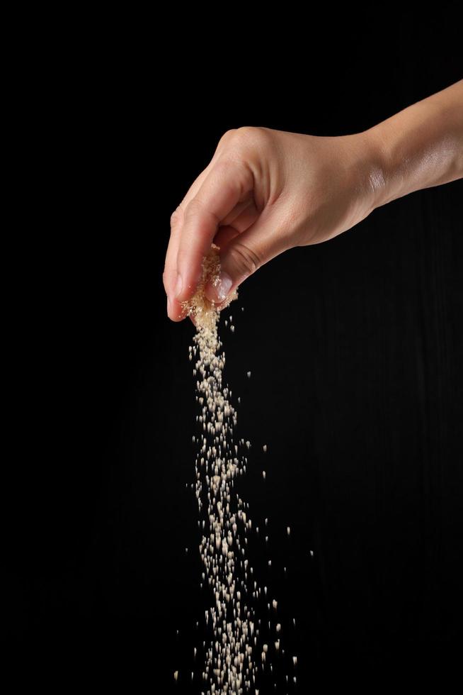 Hand bestreut braunen Zucker auf schwarzem Hintergrund foto