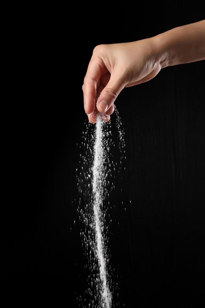 Hand bestreut braunen Zucker auf schwarzem Hintergrund foto