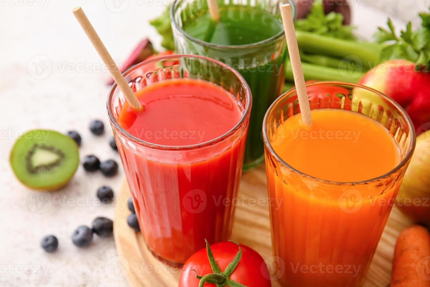 Gläser mit gesundem Saft, Obst und Gemüse auf hellem Hintergrund foto