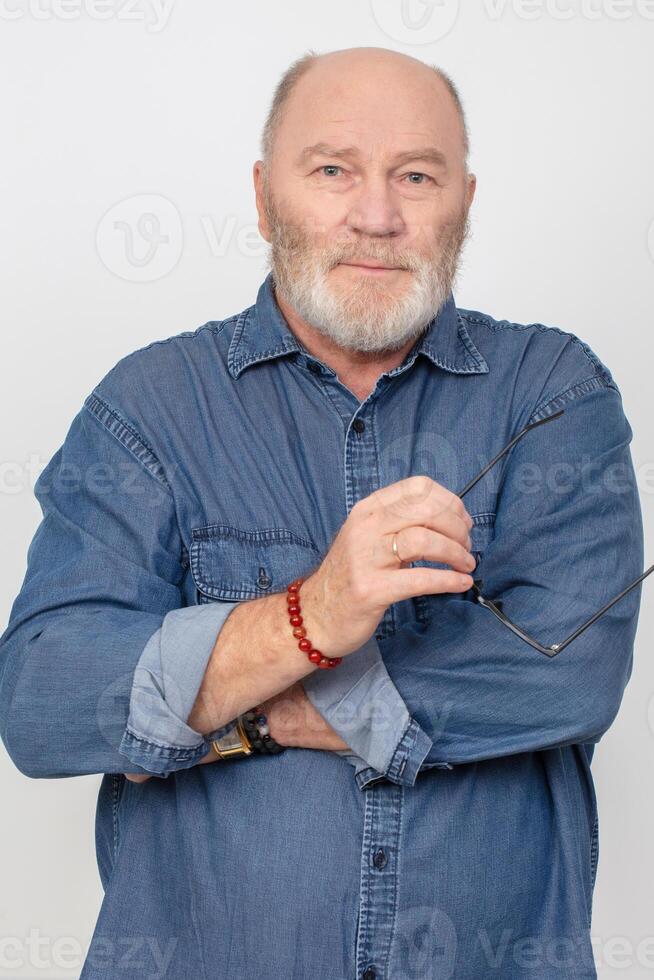 Porträt von ein attraktiv grau haarig Mann im ein Denim Hemd isoliert auf ein grau Hintergrund. bärtig Großvater von das europäisch Typ. foto