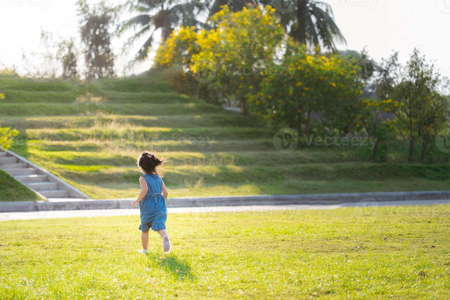 Porträt von asiatisch Kind Mädchen genießen draussen Spielzeit inmitten Natur, Laufen auf Grün Gras im das Park, Rückseite zurück Sicht, im Sommer- oder Frühling Zeit, Lauf im das Grün Felder, schließen zu Natur. foto