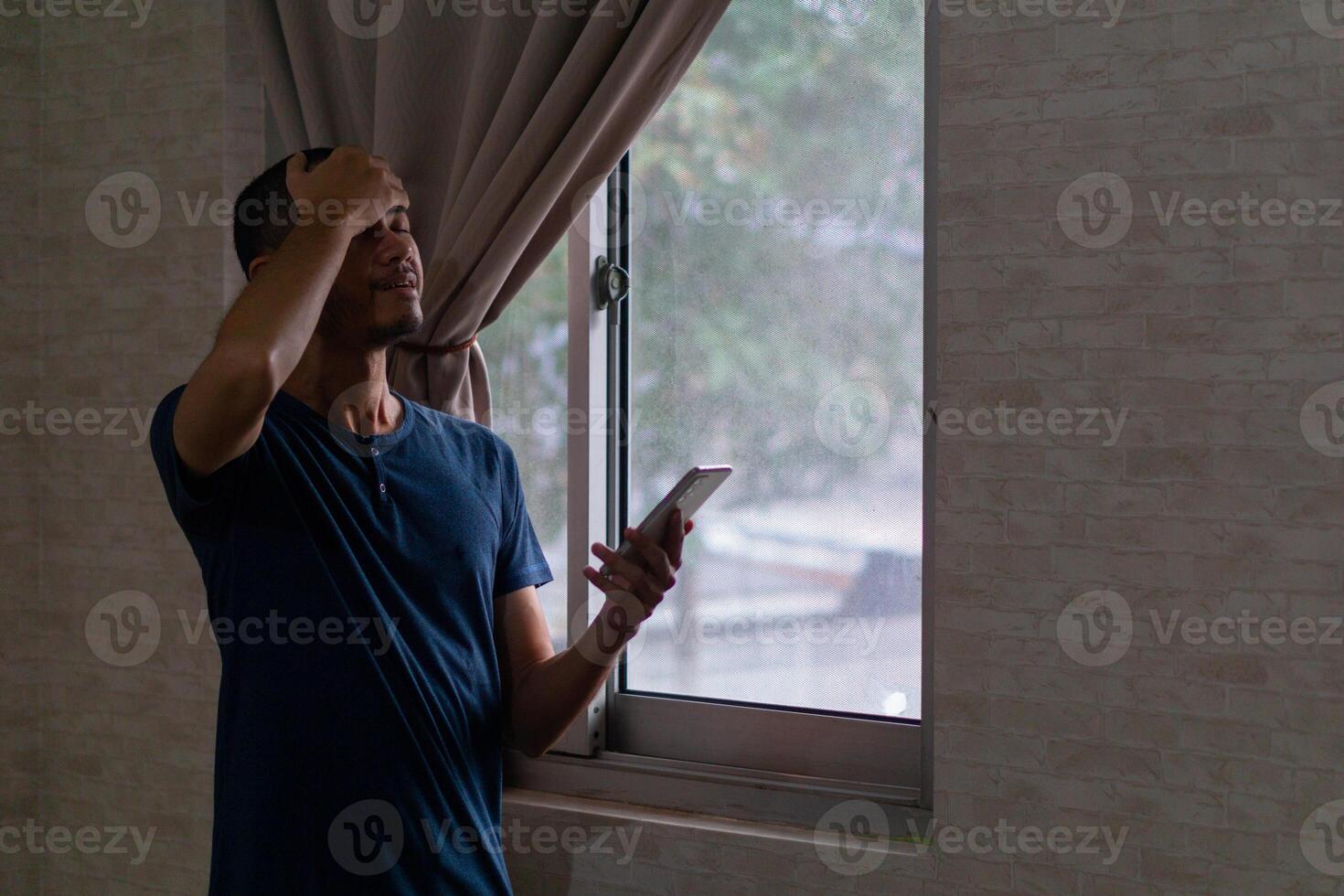 jung asiatisch Mann mit Smartphone betont mit Hand auf Kopf neben von Fenster foto