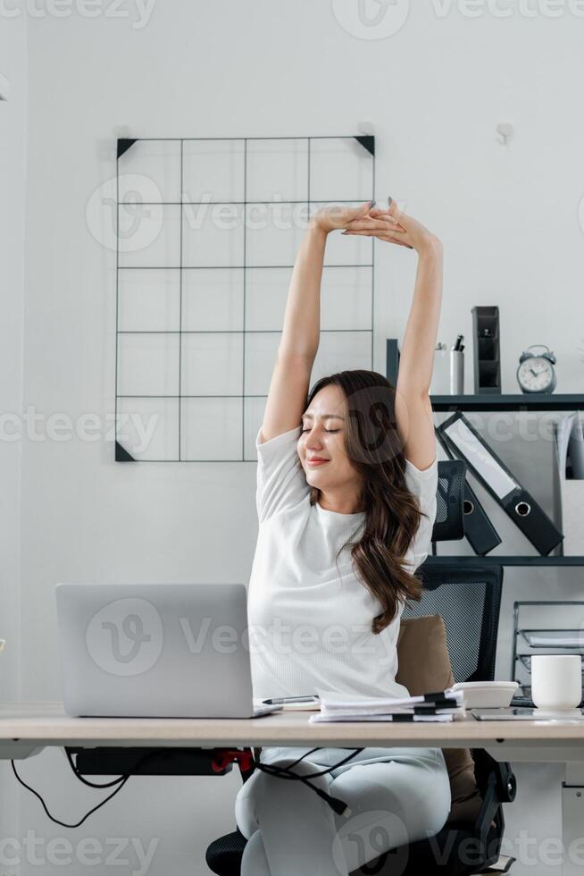 Geschäftsfrau nimmt ein Moment zu strecken und entspannen beim ihr Schreibtisch, im ein hell und luftig Büro Raum. foto