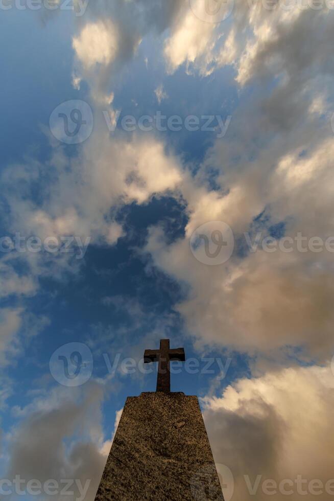 Abonnieren von Stein Grab Kreuz gegen das Hintergrund von ein Blau Abend Himmel mit Wolken foto