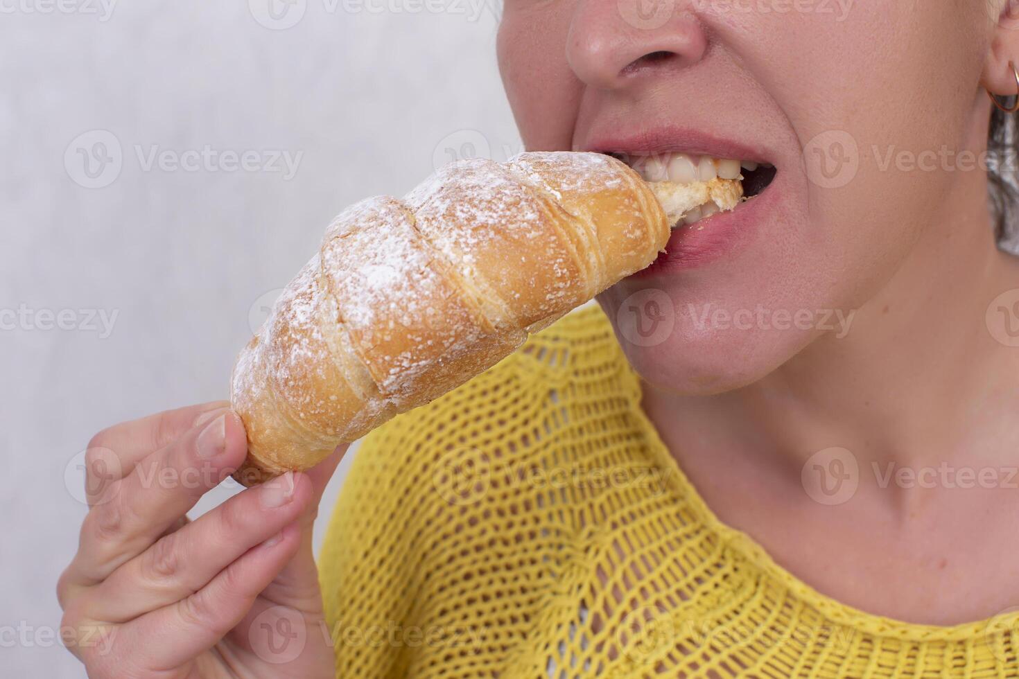 ein Frau, deren Gesicht ist nicht sichtbar, isst ein Croissant. foto