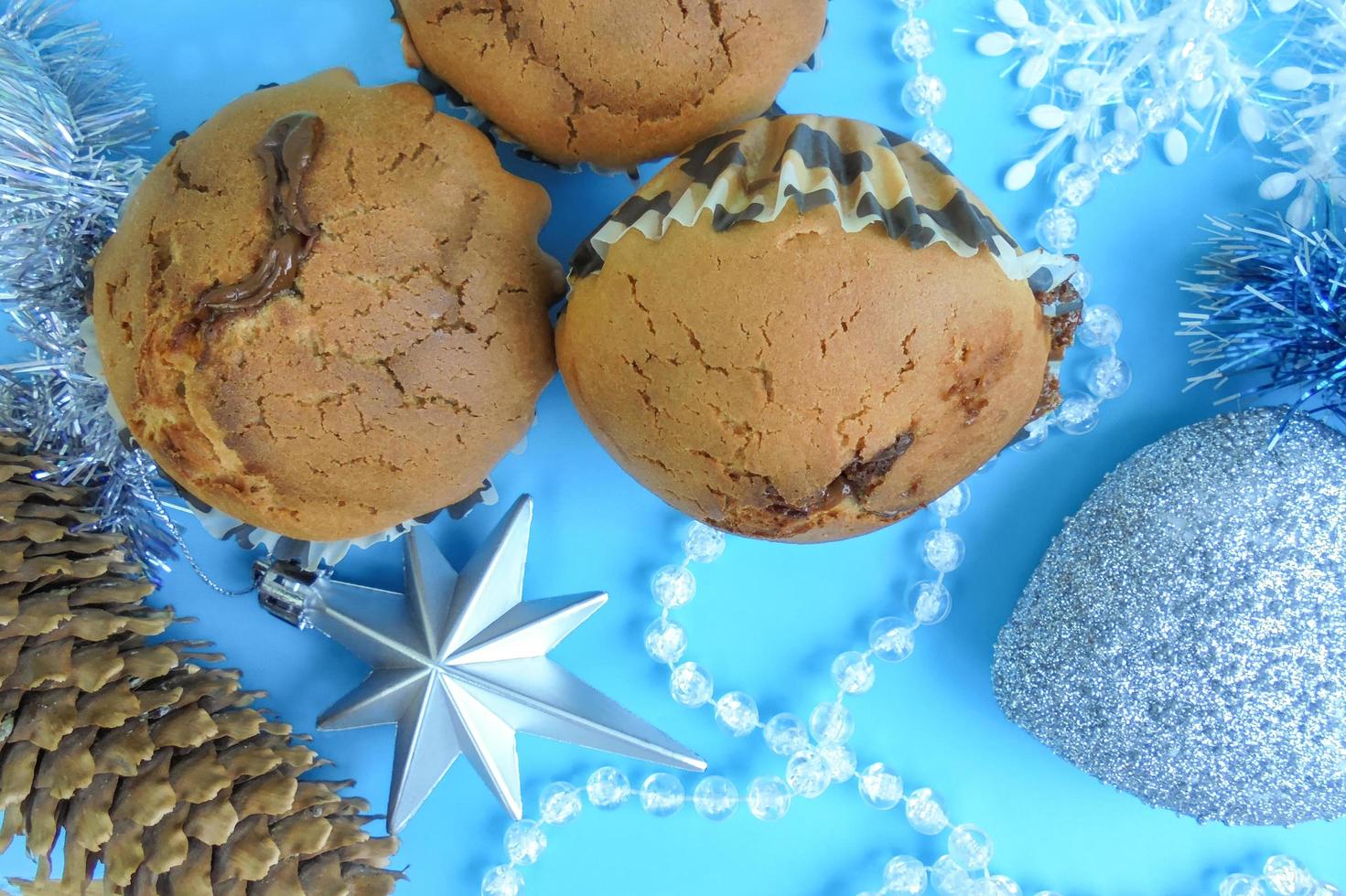 Drei Muffins mit Schokoladenfüllung, einen silbernen Weihnachtsstern und einen Tannenzapfen auf blauem Grund. Sicht von oben foto