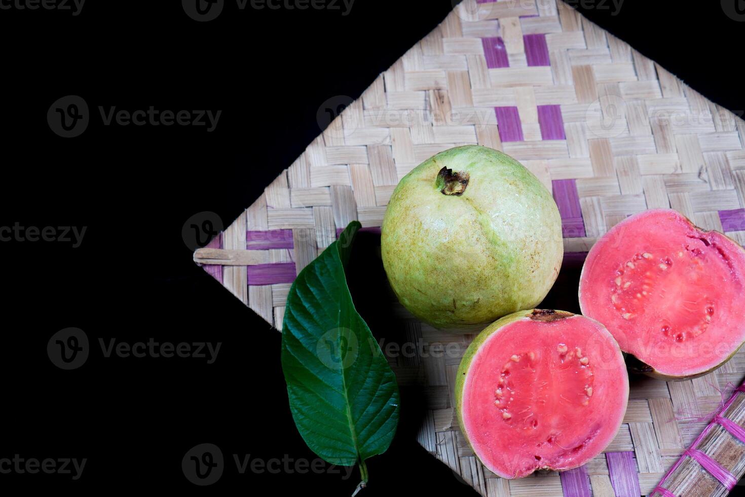 Guave isoliert. Sammlung von rot fleischig Guave Obst mit gelblich Grün Haut und Blätter isoliert auf schwarz Hintergrund mit gewebte Bambus. foto