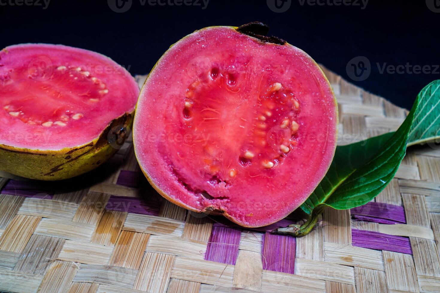 Guave isoliert. Guave Obst mit rot Fleisch mit gelblich Grün Haut und Blätter isoliert auf ein schwarz Hintergrund mit gewebte Bambus wie ein Base. foto