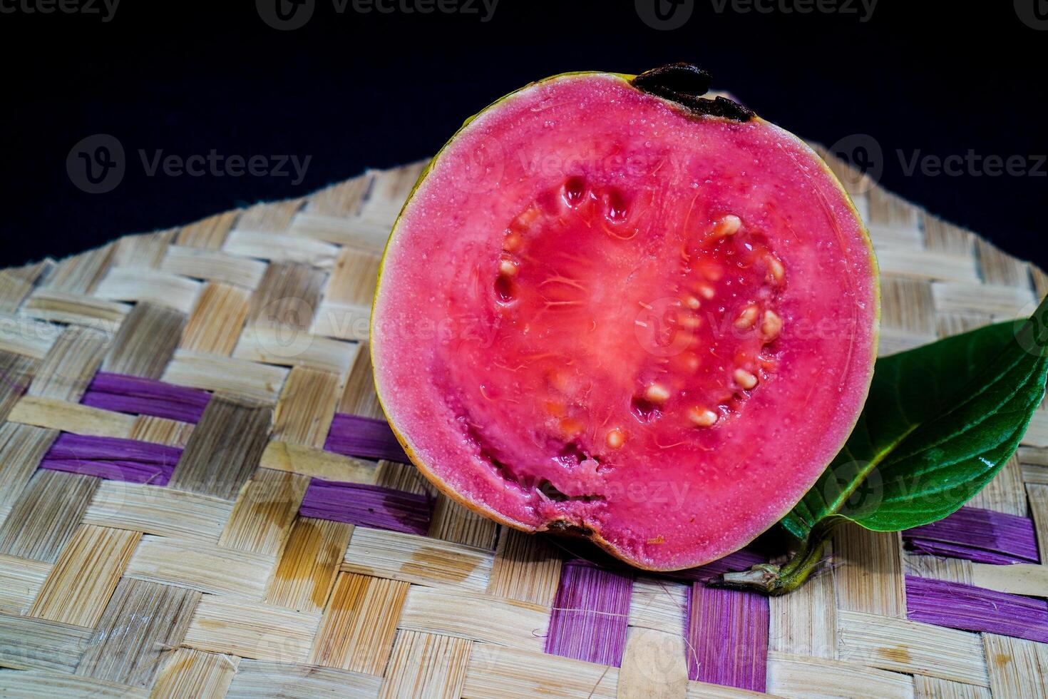 Guave isoliert. Guave Obst mit rot Fleisch mit gelblich Grün Haut und Blätter isoliert auf ein schwarz Hintergrund mit gewebte Bambus wie ein Base. foto