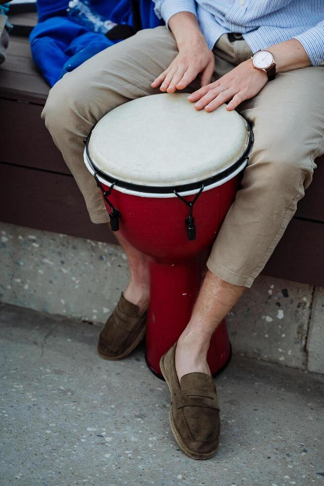 ein Weiß Kerl Theaterstücke ein Trommel, ein Straße Jazz Musiker auf ein Djemba, ein rot Musical Instrument, braun Macasins, ein Uhr auf seine Arm. foto