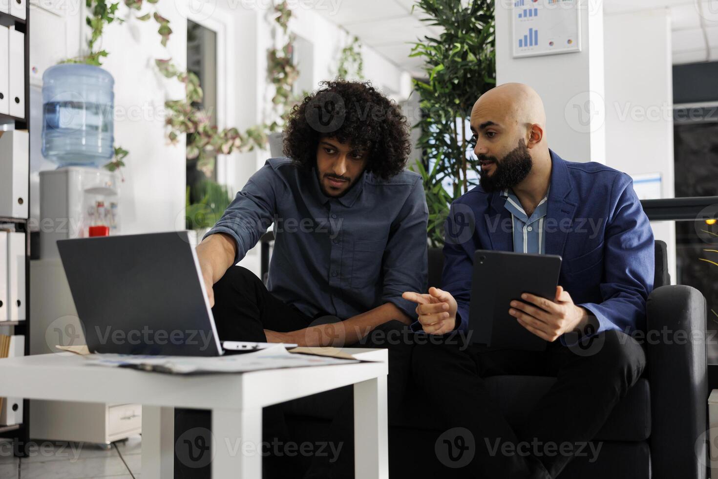 Unternehmer und Kollege diskutieren Projekt während Analysieren Daten auf Laptop im Geschäft Büro. arabisch Angestellte Planung Produkt Beförderung Strategie zusammen im Coworking Raum foto