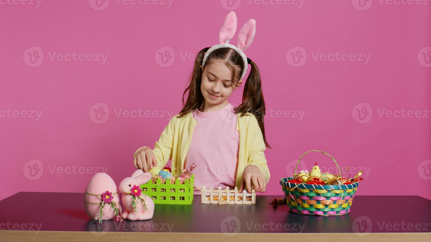 lächelnd glücklich Schülerin präsentieren ein handgemacht dekoriert Korb im Studio, Herstellung Ostern Urlaub Vorbereitungen gegen Rosa Hintergrund. jung Kind zeigen handgemacht Anordnungen. Kamera b. foto